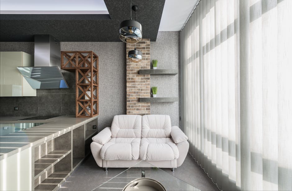 White leather sofa placed near kitchen with appliances at wall with decorative elements in modern apartment with tulle on window