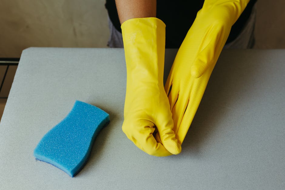 Close-up of hands in yellow gloves preparing for cleaning with blue sponge.